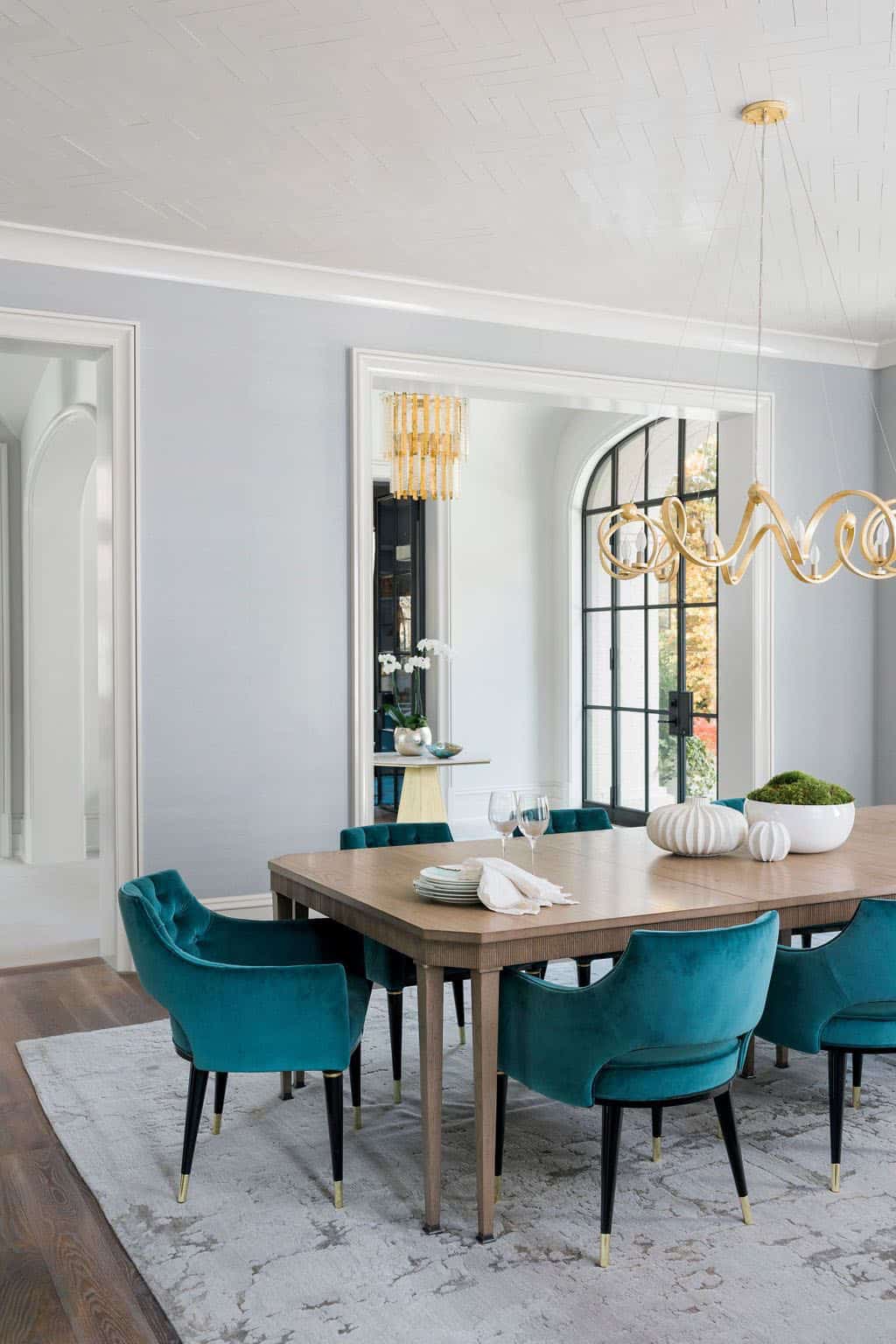 Modern English country dining room with teal velvet chairs, ash wood table and gold sculptural chandelier in Georgia