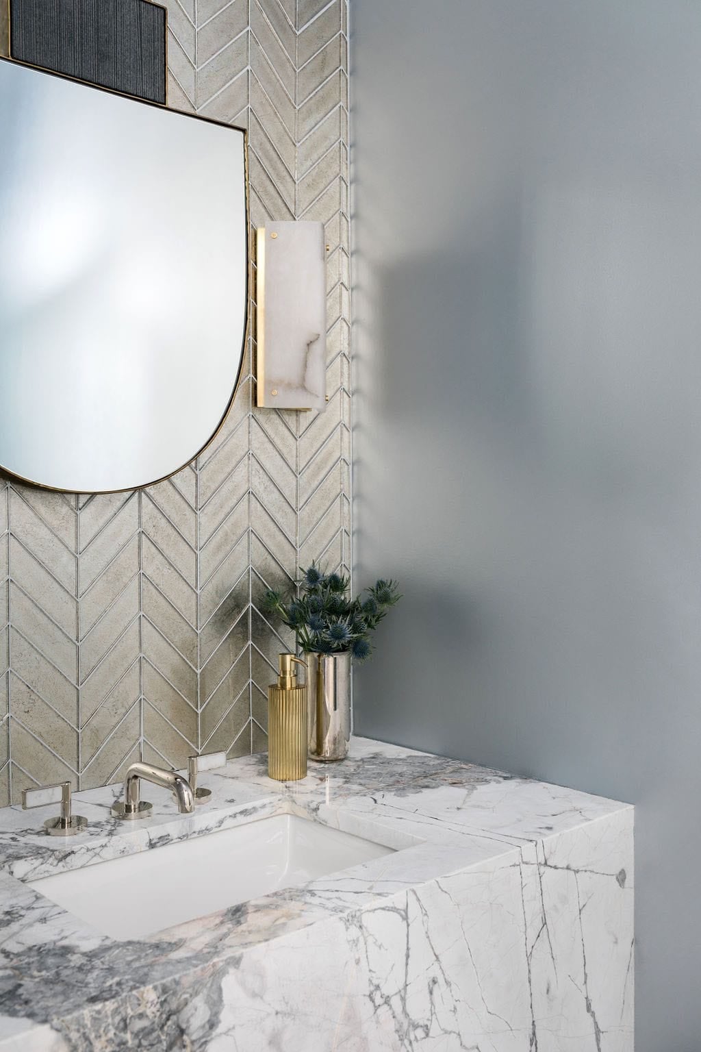 Modern English country powder room with marble waterfall vanity, chevron tile backsplash and brass sconce in Georgia