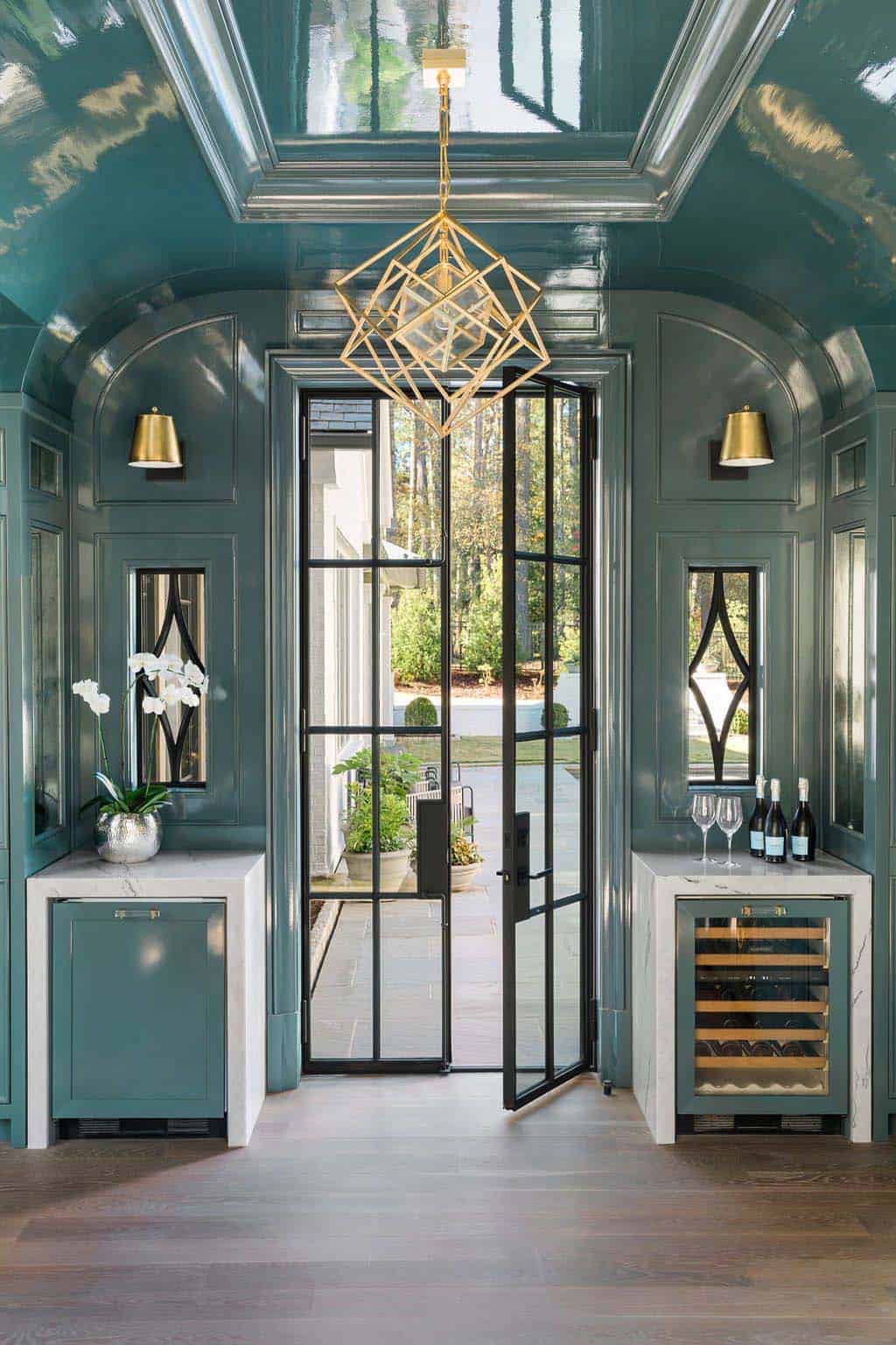 Modern English country interior bar with teal lacquer walls, arched ceiling, gold geometric chandelier and steel-framed doors in Georgia
