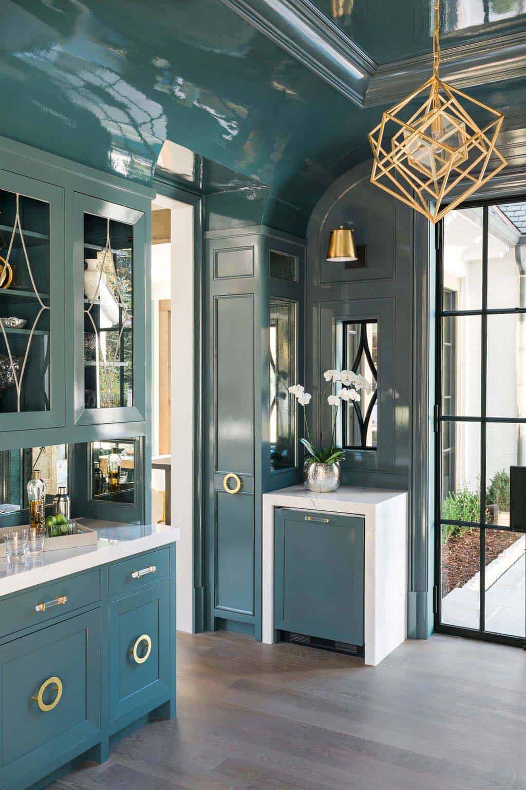 Modern English country interior bar with teal lacquered cabinetry, brass hardware, glass-front cabinets and gold chandelier in Georgia