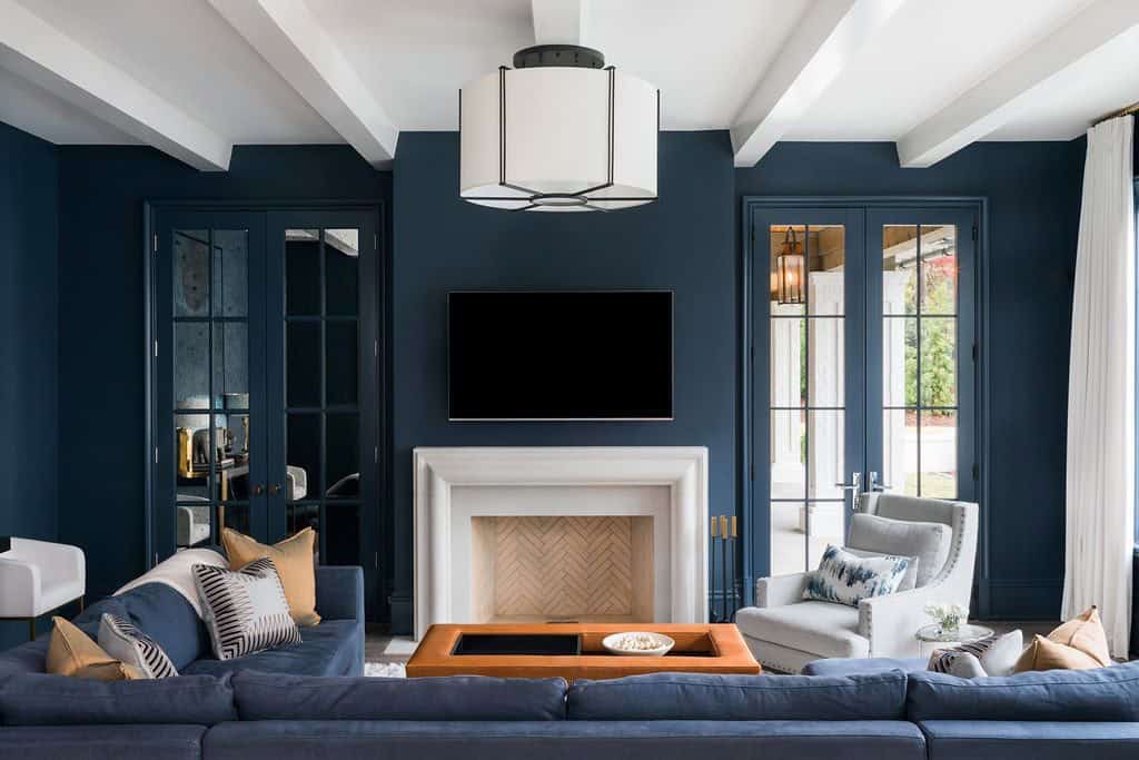 Modern English country family room with navy blue walls, white fireplace surround, exposed beams and french doors in Georgia