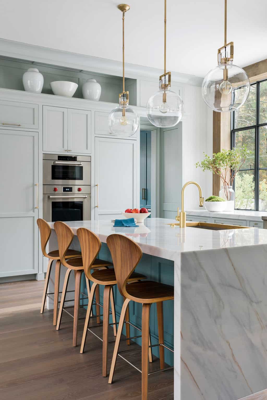 Modern English country kitchen with sage green perimeter cabinetry, teal island, Cherner bar stools and globe pendant lights in Georgia