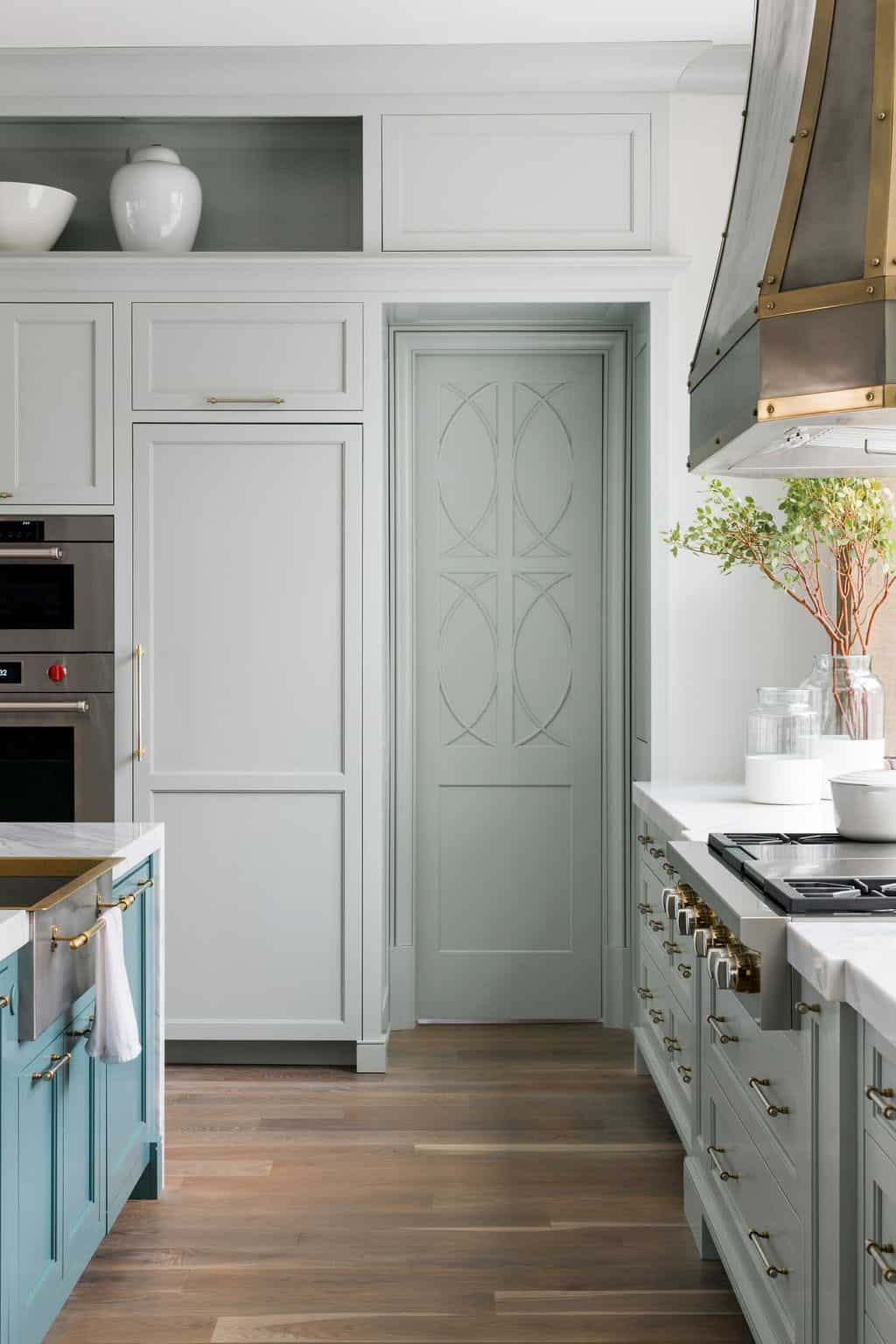 Modern English country kitchen with sage green cabinetry, decorative pantry door, custom zinc range hood and brass hardware in Georgia