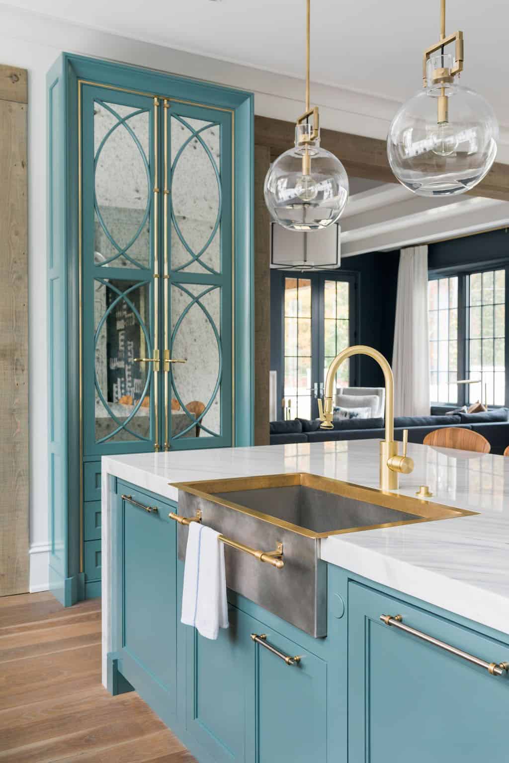Modern English country kitchen teal island with custom brass farmhouse sink, antique mirror cabinet doors and globe pendant lights in Georgia
