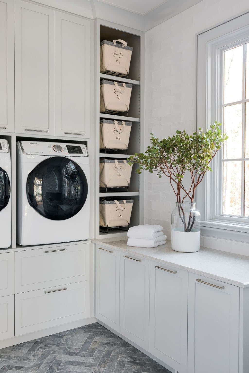 Modern English country laundry room with white cabinetry, built-in laundry basket shelving and herringbone slate tile floor in Georgia
