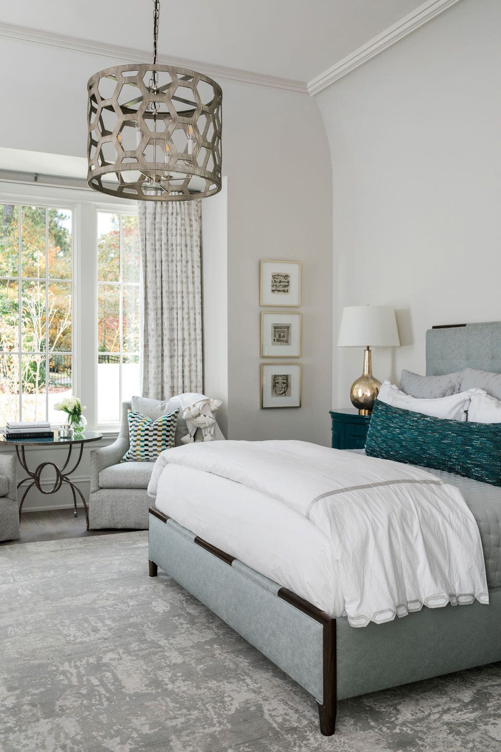 Modern English country primary bedroom with upholstered blue bed, teal lacquer nightstand, honeycomb chandelier and steel-framed windows in Georgia