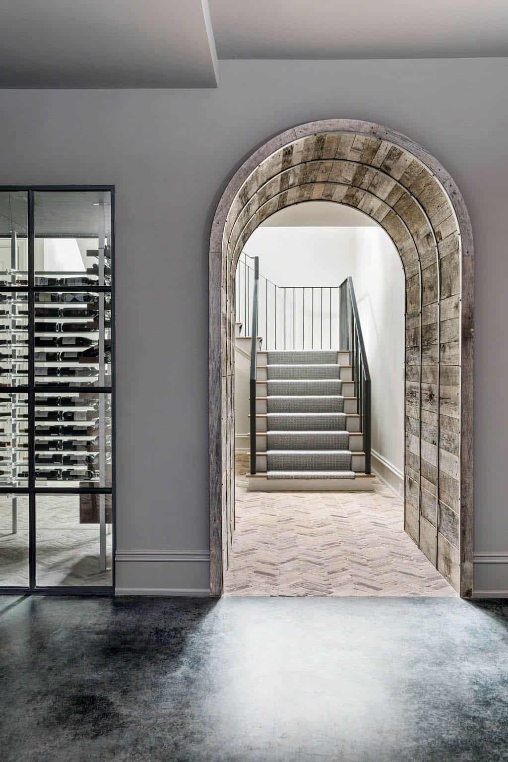 Modern English country basement with reclaimed wood arched doorway, glass wine cellar and herringbone brick floor in Georgia