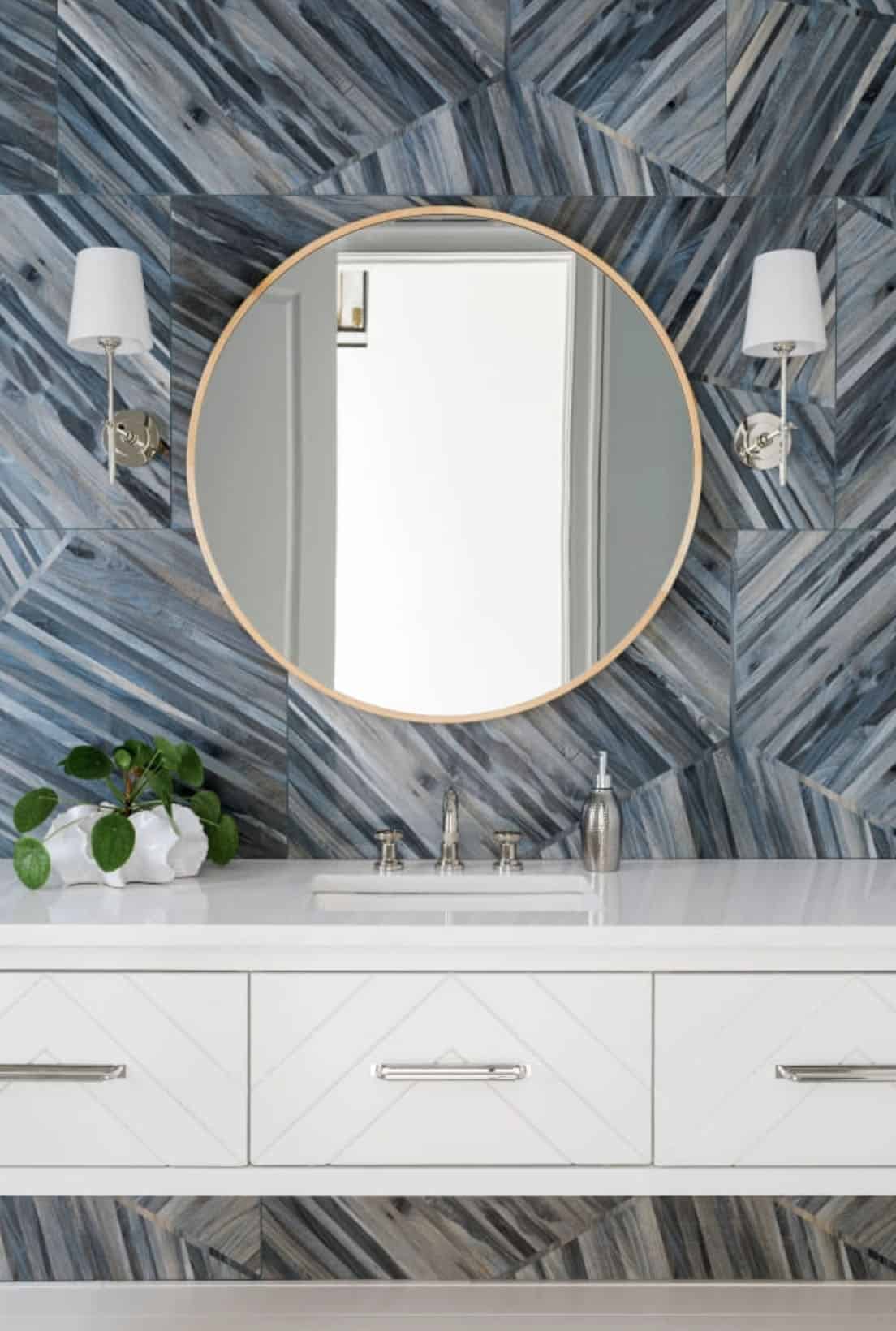 Modern English country guest bathroom with bold blue chevron tile wall, round gold mirror and white floating vanity in Georgia