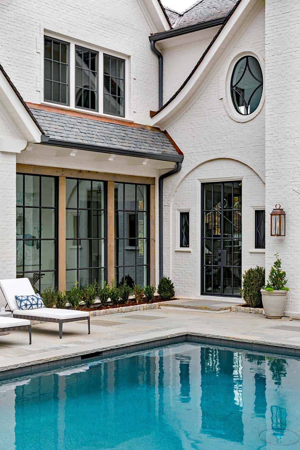 Modern English country house pool terrace with white painted brick, cedar-framed steel windows, oval window detail and chaise lounges in Georgia
