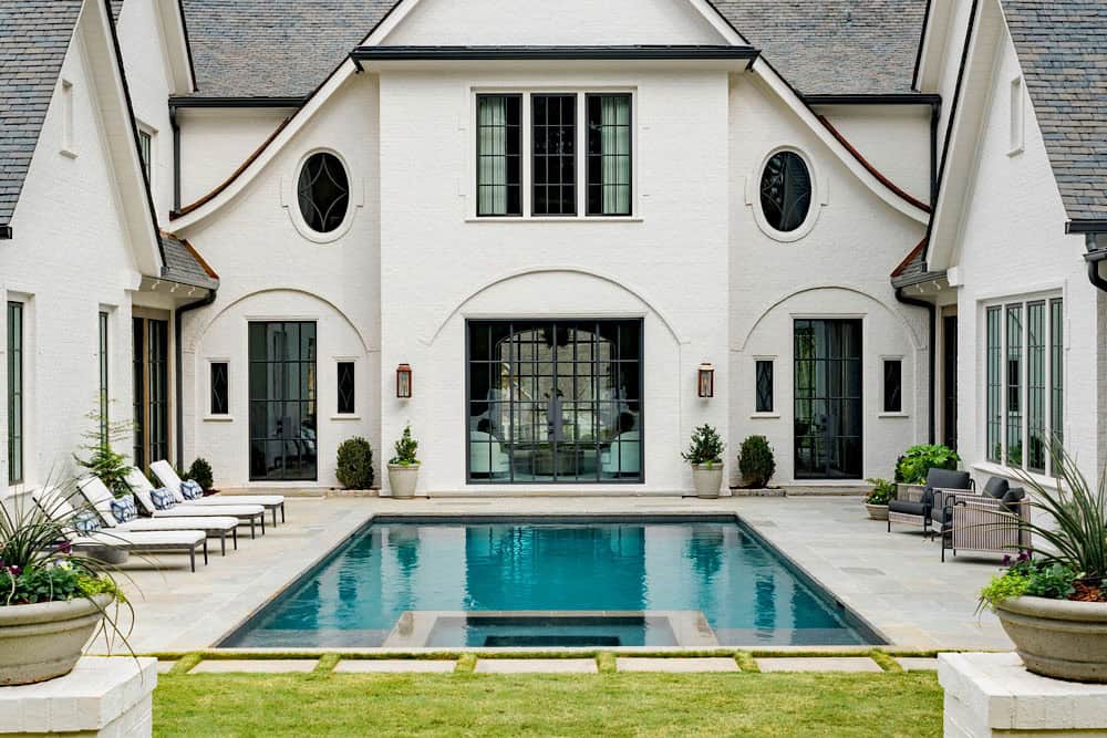 Modern English country house rear exterior with U-shaped pool terrace, arched steel-framed doors, oval windows and chaise lounges in Georgia