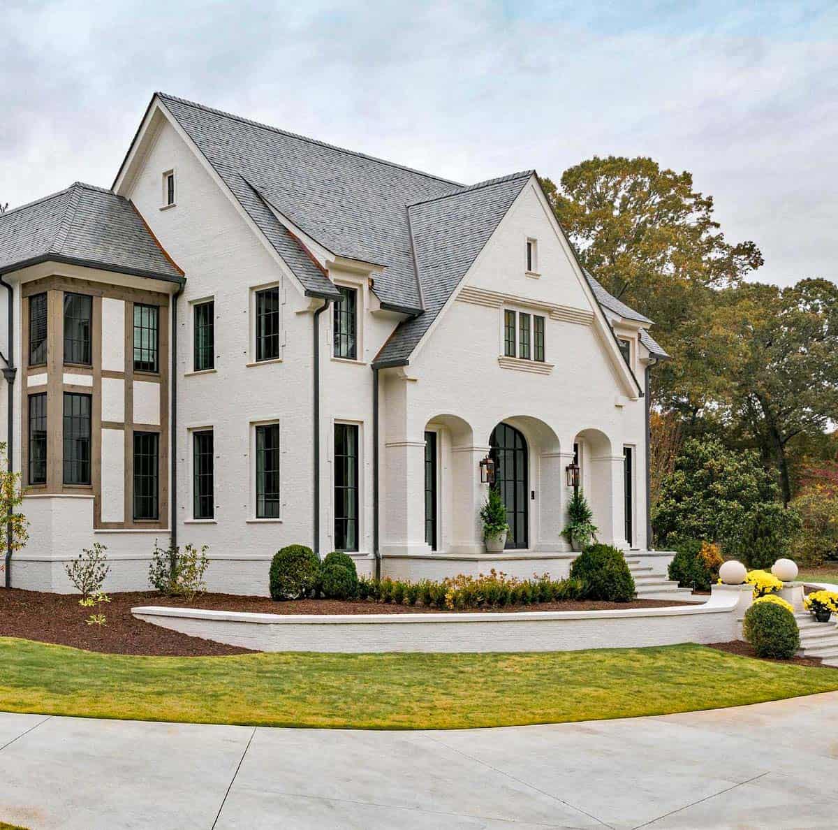 Modern English country house front exterior with white painted brick, arched entry loggia, cedar-framed window wall and circular driveway in Georgia