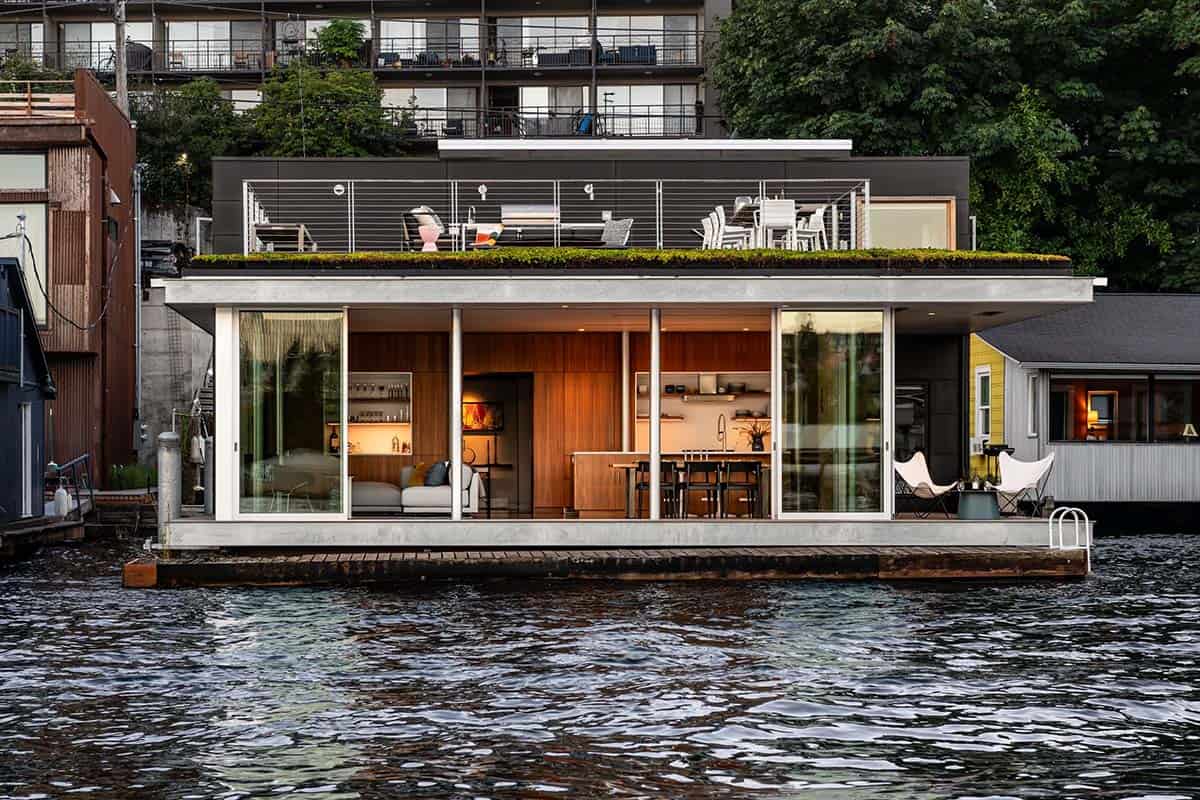 Floating home water-facing facade at dusk with green roof and open living spaces