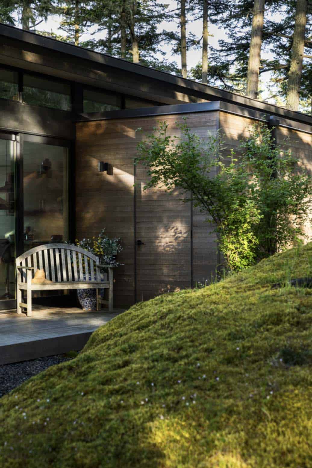 Weathered wood bench on concrete deck beside cedar-clad exterior wall with sliding glass door