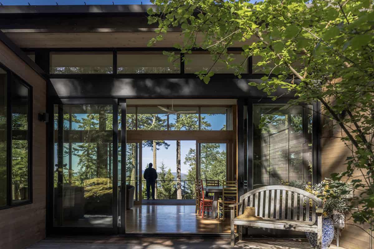 Covered entry courtyard with floor-to-ceiling glass walls framing forest and water views beyond