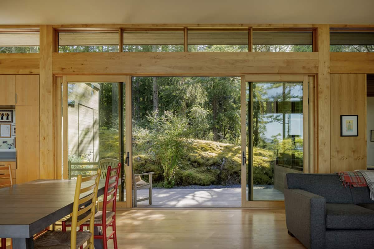 Dining and living room with sliding glass doors opening to moss-covered courtyard between home wings
