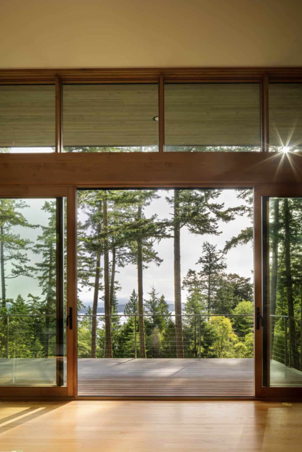 Bedroom sliding glass door framing tall Pacific Northwest conifers and a glimpse of water beyond