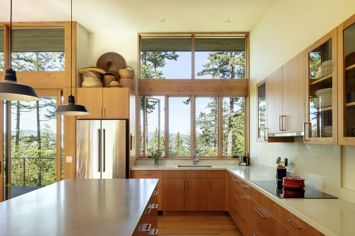 Kitchen with warm wood cabinetry, stainless countertops, pendant lights, and tree-framed water views