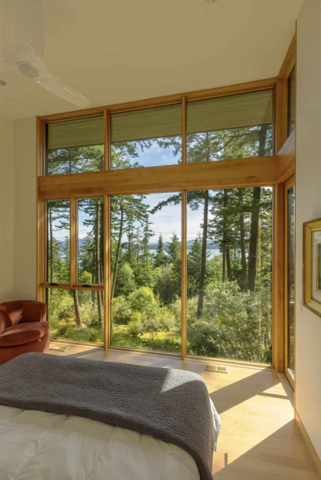 Primary bedroom with panoramic corner windows overlooking forested slope and distant water views