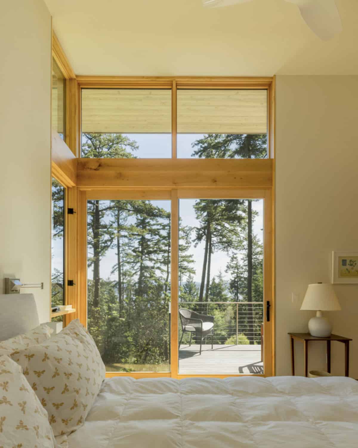 Guest bedroom with sliding glass door and transom windows opening to tree-canopy deck
