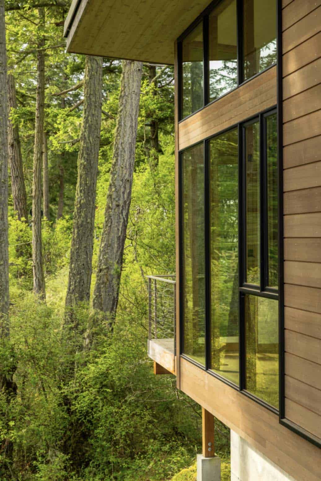 Cedar siding exterior detail with black-framed windows reflecting forest canopy and cable-rail deck