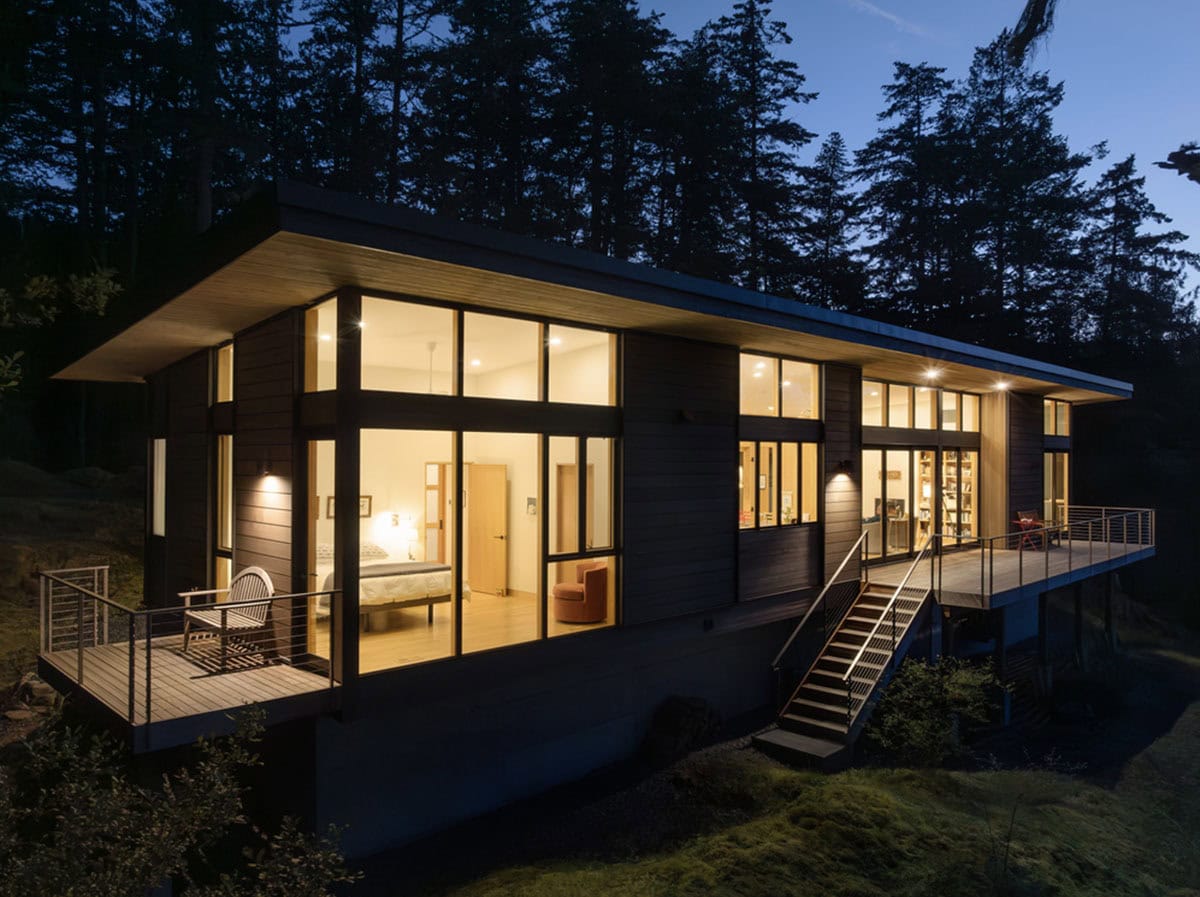 Dusk exterior showing illuminated bedrooms and living areas with cable-railed decks on hillside