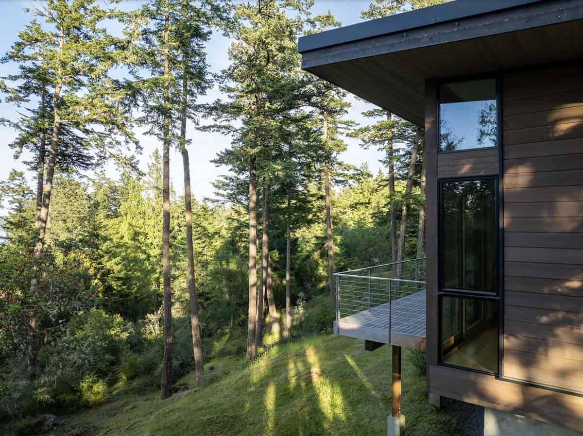 Cantilevered deck with cable railing projecting over forested hillside beside dark cedar-clad exterior wall