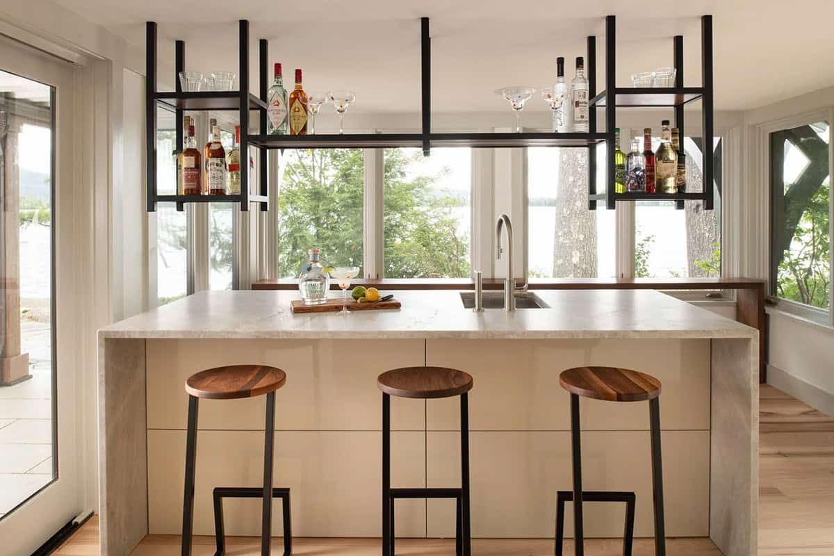 Bar area with marble island, black steel hanging shelves with liquor bottles, and lake views through windows