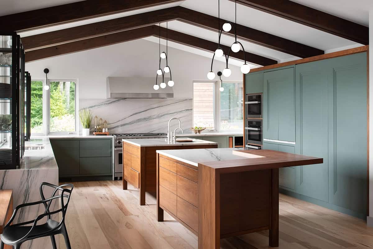 Open kitchen with vaulted ceiling, dark wood beams, sage green cabinets, walnut island, and marble backsplash