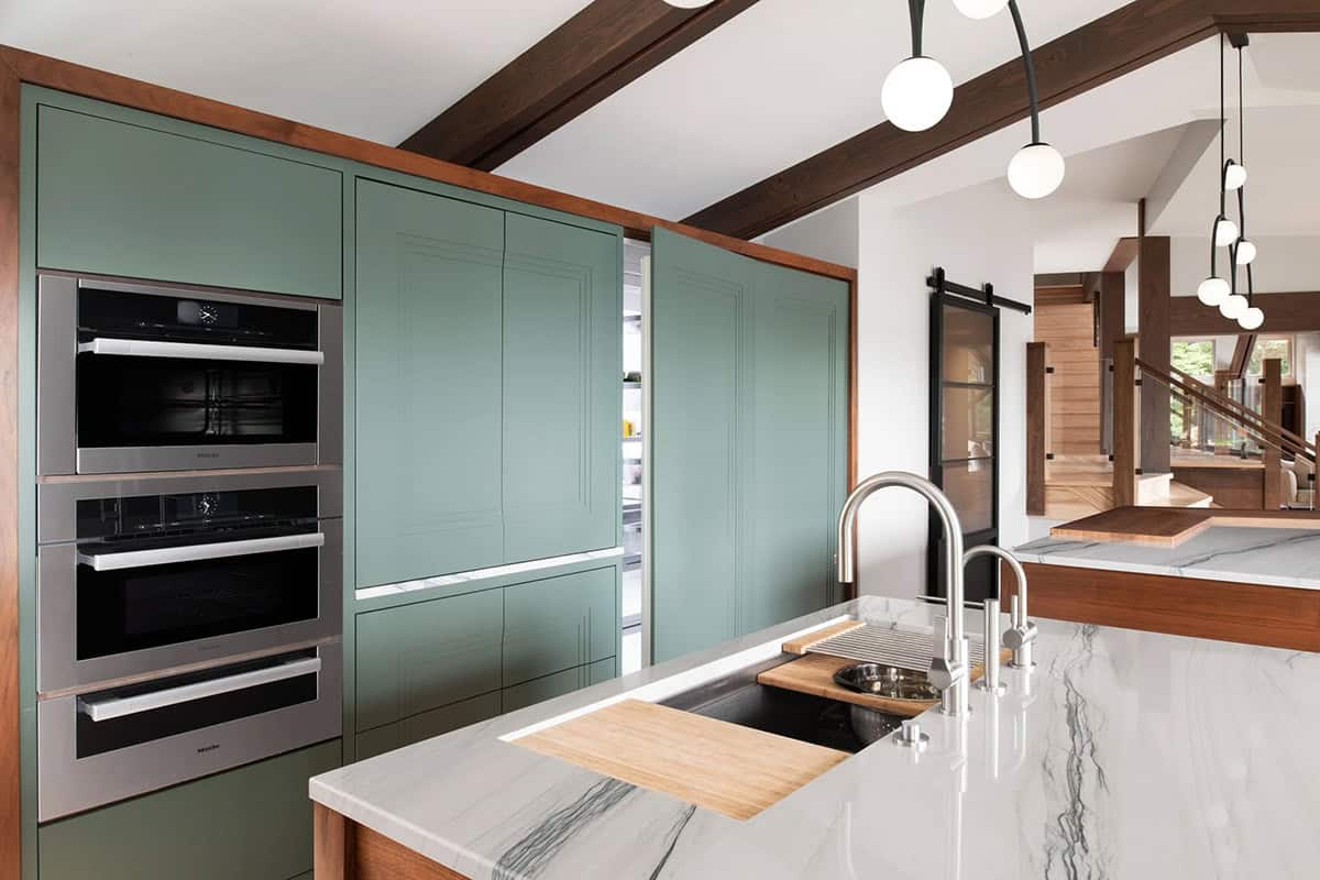 Kitchen detail showing Miele wall ovens, sage green cabinetry, marble countertop with sink, and barn door