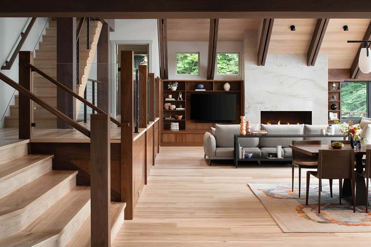 Open-plan interior showing staircase, living room with fireplace, built-in walnut shelving, and dining area
