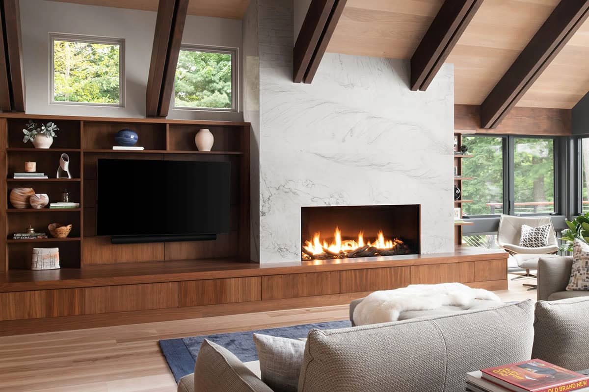 Living room with walnut built-ins, large TV, marble fireplace surround, and gas fireplace with wood logs