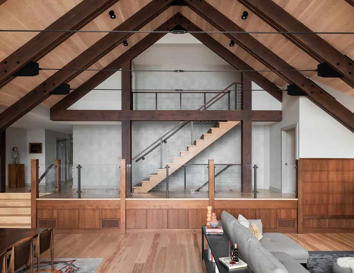 Vaulted great room with dark wood A-frame beams, floating staircase with cable railing, and walnut millwork