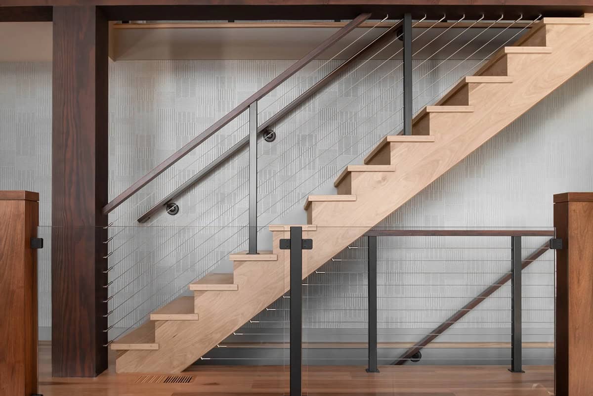 Floating maple staircase with black steel cable railing against textured gray wallcovering