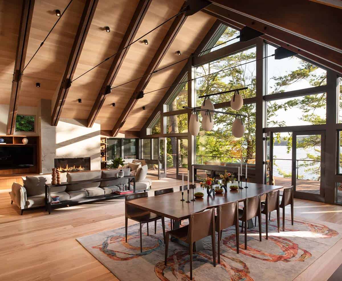 Great room with vaulted ceiling, floor-to-ceiling windows overlooking lake, dining table, and gas fireplace
