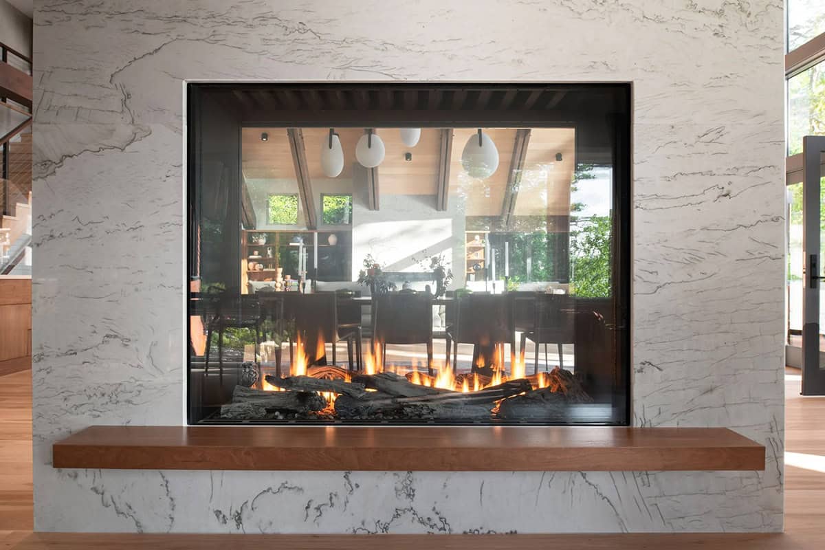 Double-sided see-through gas fireplace clad in dramatic white marble with walnut hearth