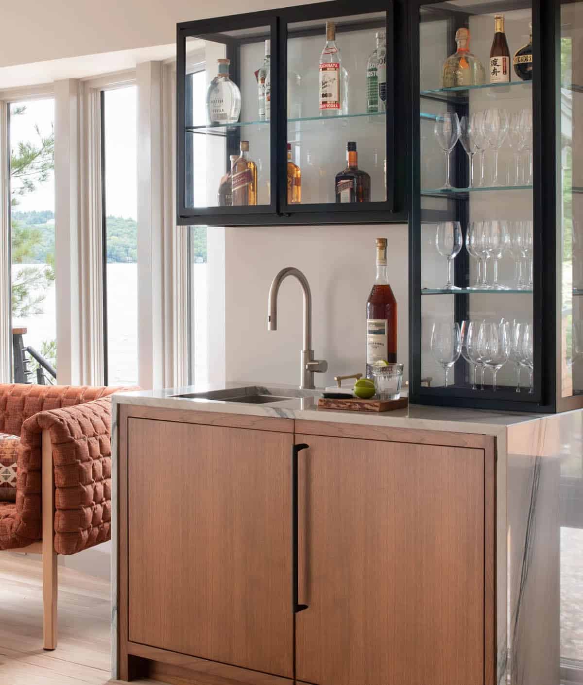 Wet bar with warm wood cabinetry, marble countertop, and black steel glass-front liquor cabinets