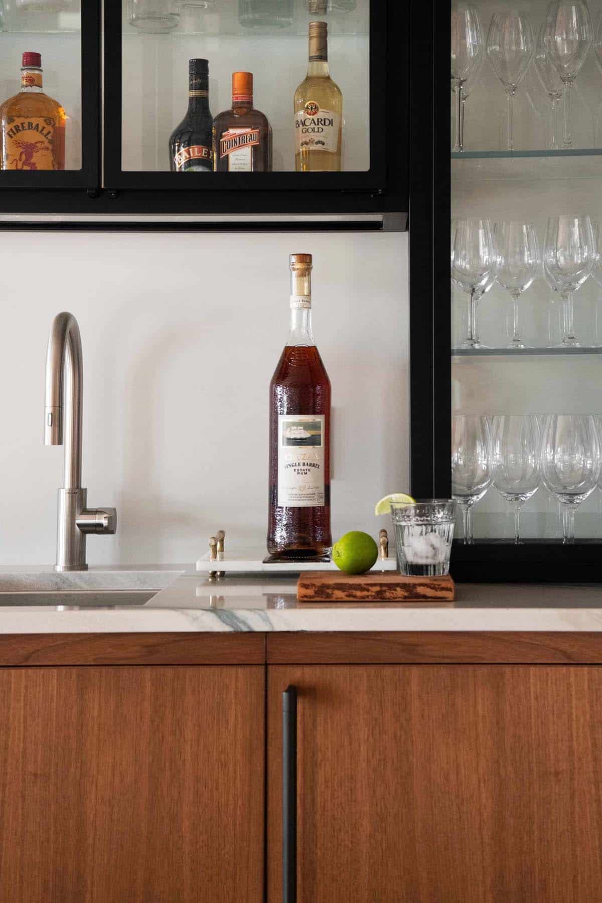 Wet bar close-up with single barrel rum bottle, lime, marble counter, and glass-front cabinet