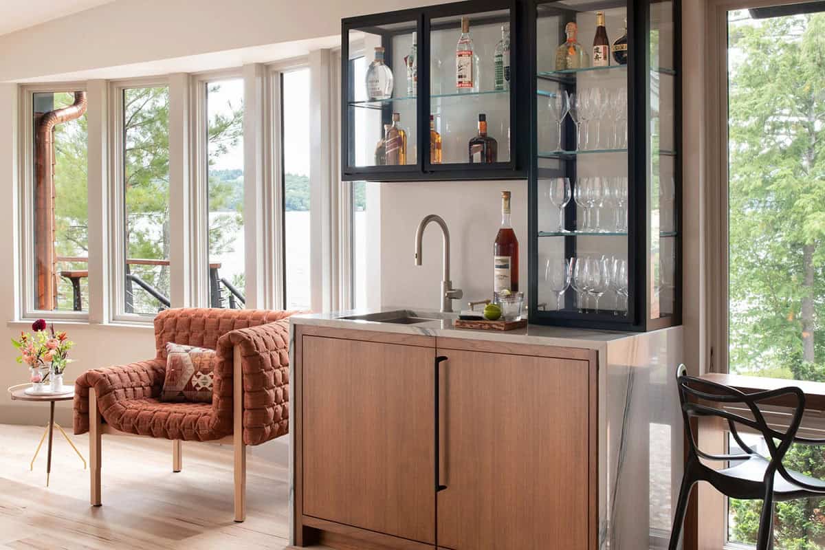 Wet bar with oak cabinetry, black steel display cabinets, and lake views through surrounding windows