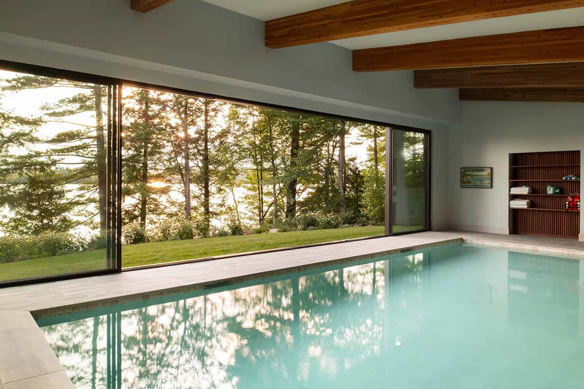 Indoor lap pool reflecting trees through oversized sliding glass wall at golden hour