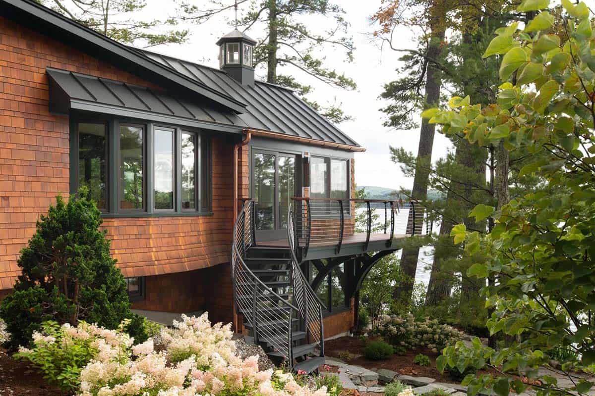 Cedar-shingled lakehouse exterior with metal roof, spiral staircase, and elevated deck overlooking lake