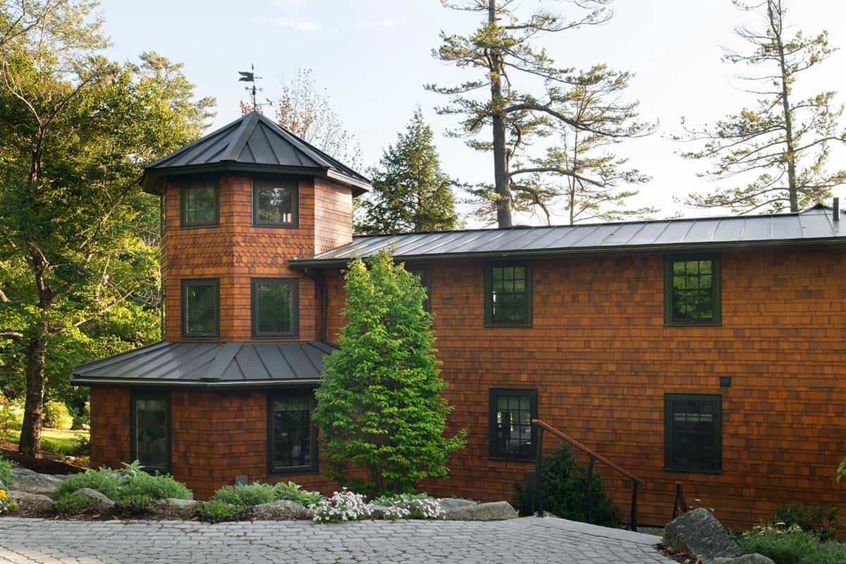 Cedar-shingled home with distinctive octagonal tower, metal roof, weather vane, and cobblestone driveway