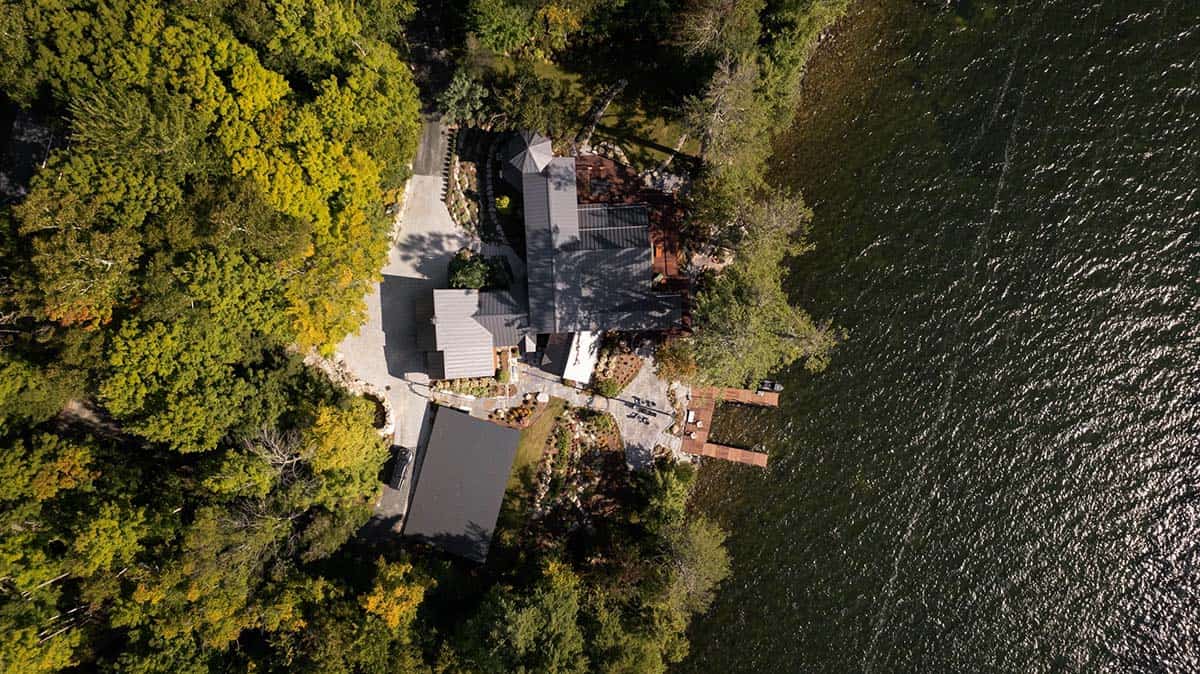 Bird's-eye drone view of full lakehouse property with metal roofs, driveway, dock, and lake