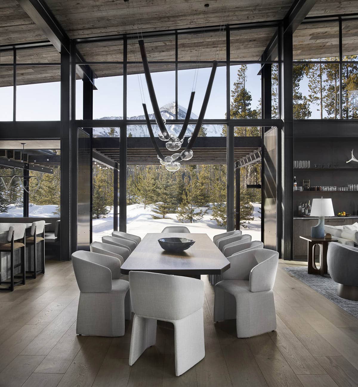 Dining room with floor-to-ceiling steel-framed windows framing snowy Lone Peak views and sculptural glass pendant