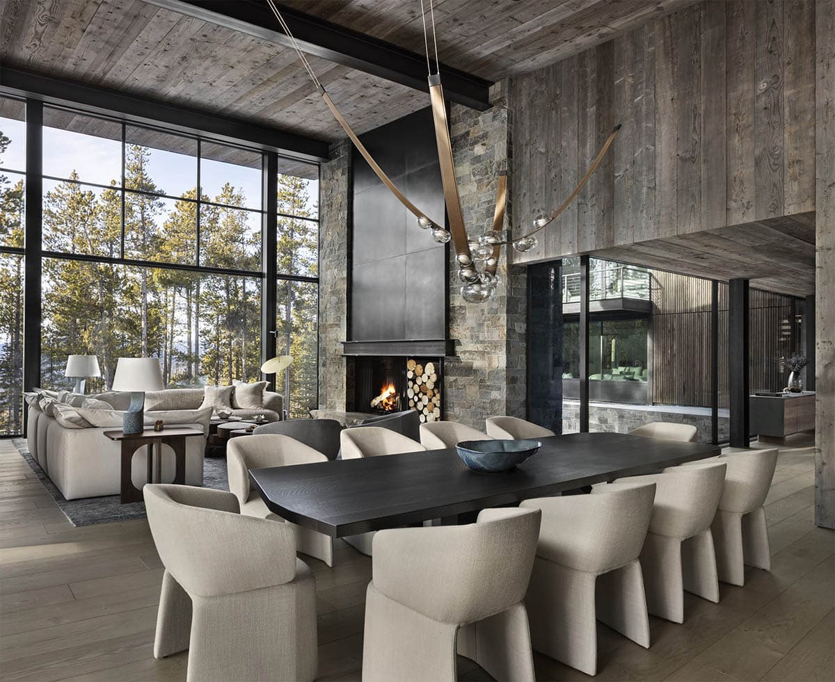 Open-plan living and dining area with reclaimed wood ceiling, stone fireplace, and sculptural brass chandelier