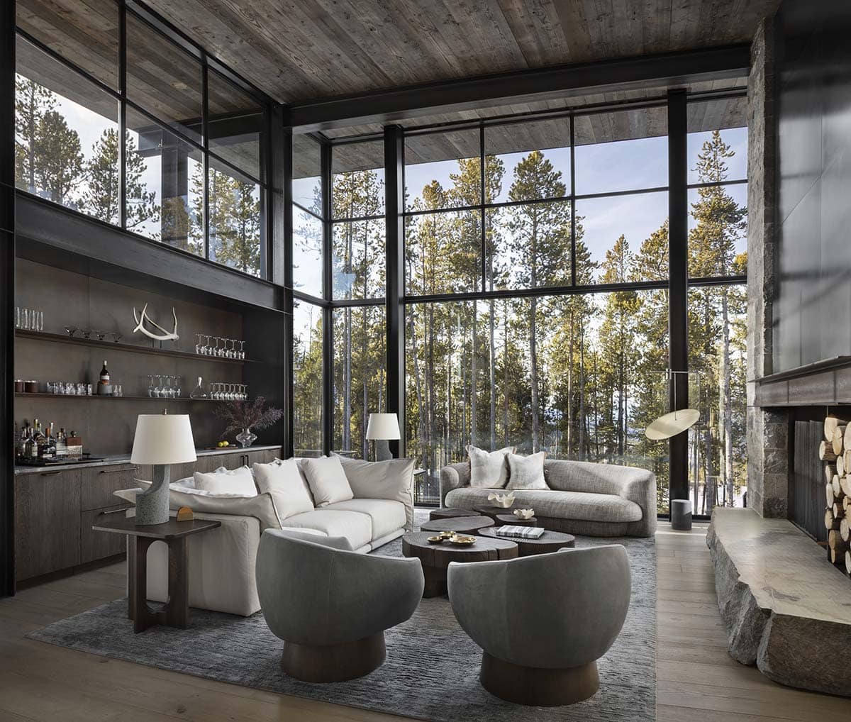 Double-height living room with floor-to-ceiling black steel windows, stone fireplace, and organic coffee tables