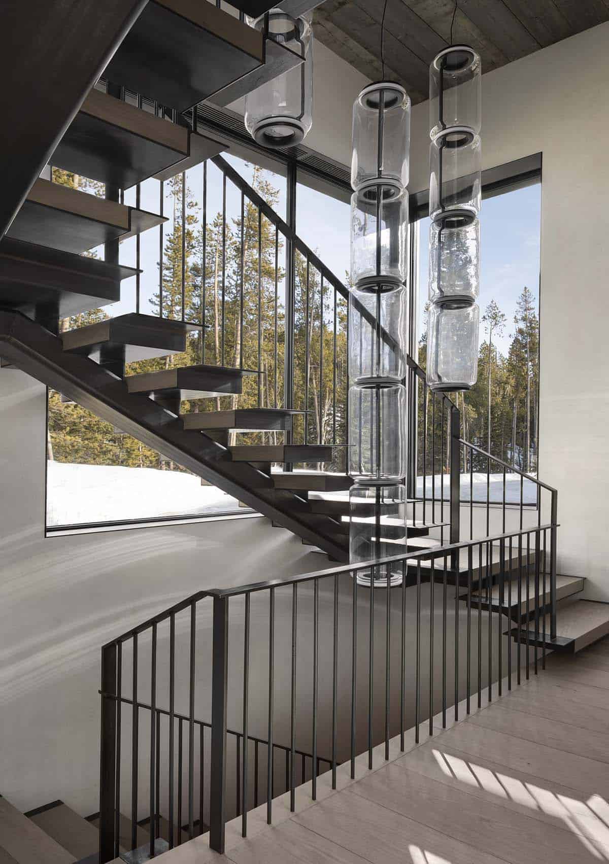 Floating steel staircase with vertical rod railing and dramatic stacked glass cylinder pendants amid snowy views