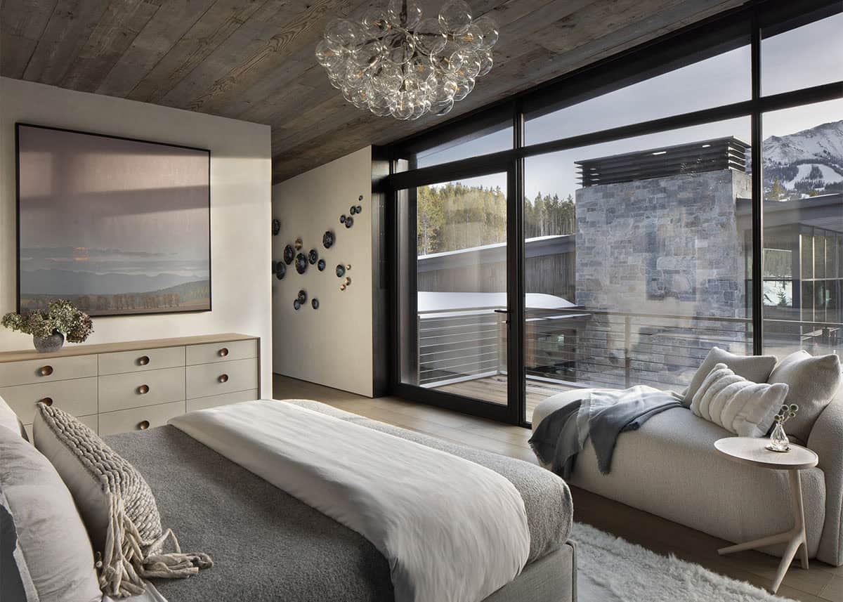 Primary bedroom with bubble glass chandelier, abstract landscape painting, chaise lounge, and snowy mountain views