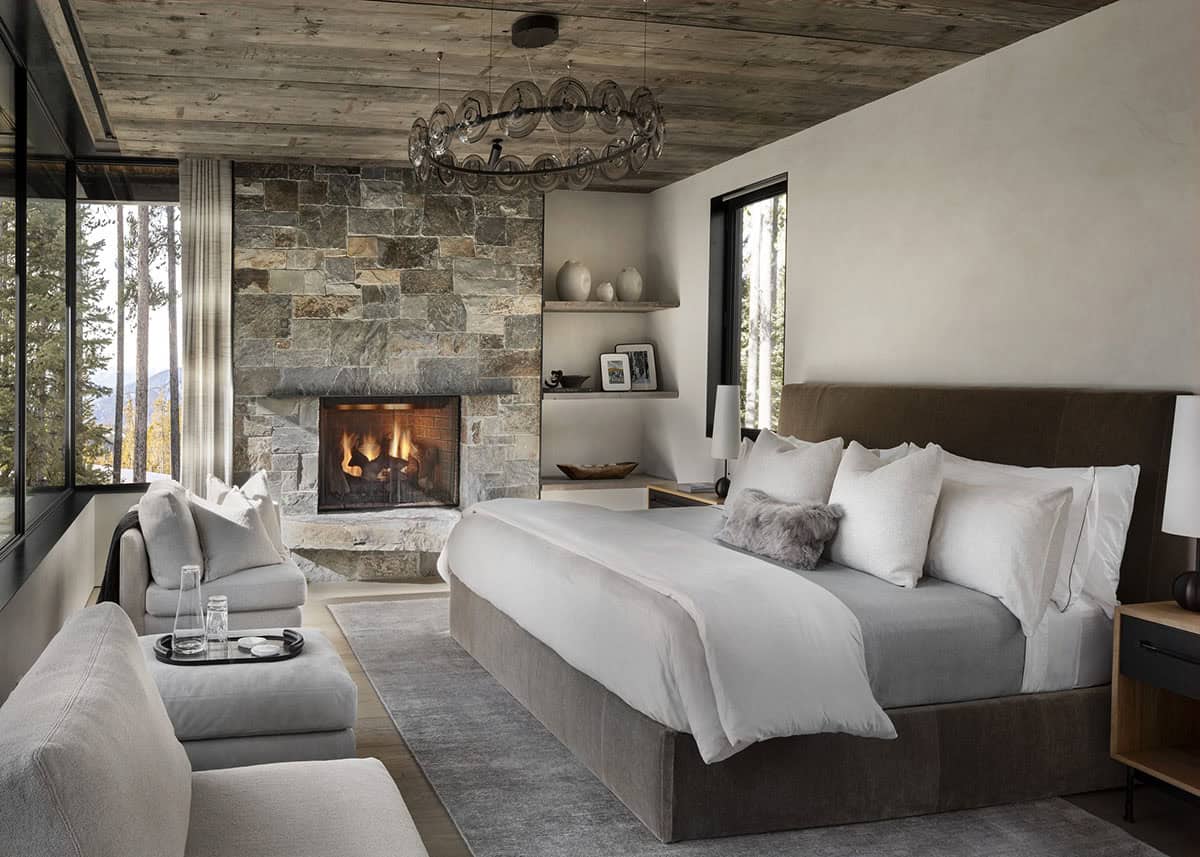 Primary bedroom with king bed, lit stone fireplace, reclaimed wood ceiling, and circular glass chandelier