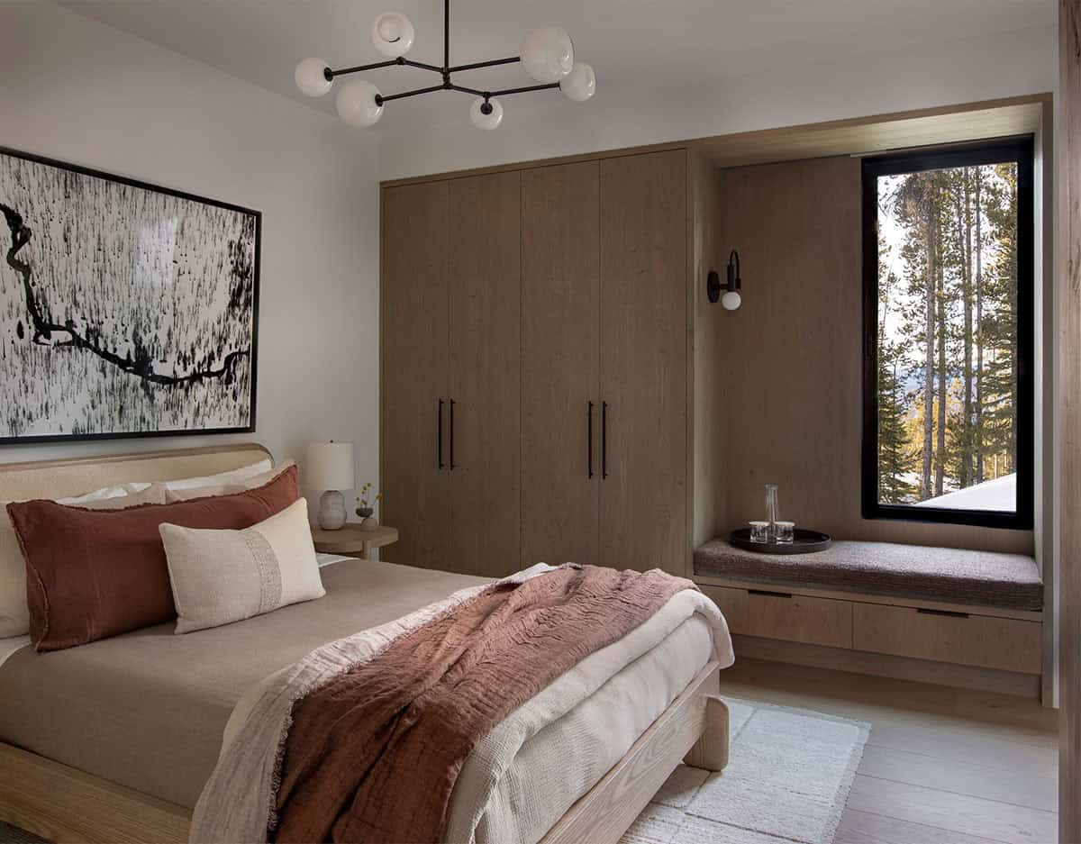 Guest bedroom with warm wood built-in wardrobe, window seat, abstract art, and forest views