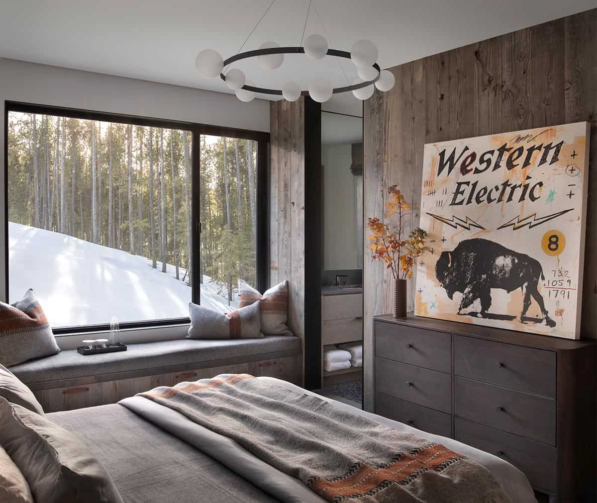 Guest bedroom with reclaimed wood wall, window seat, western bison artwork, and snowy forest view
